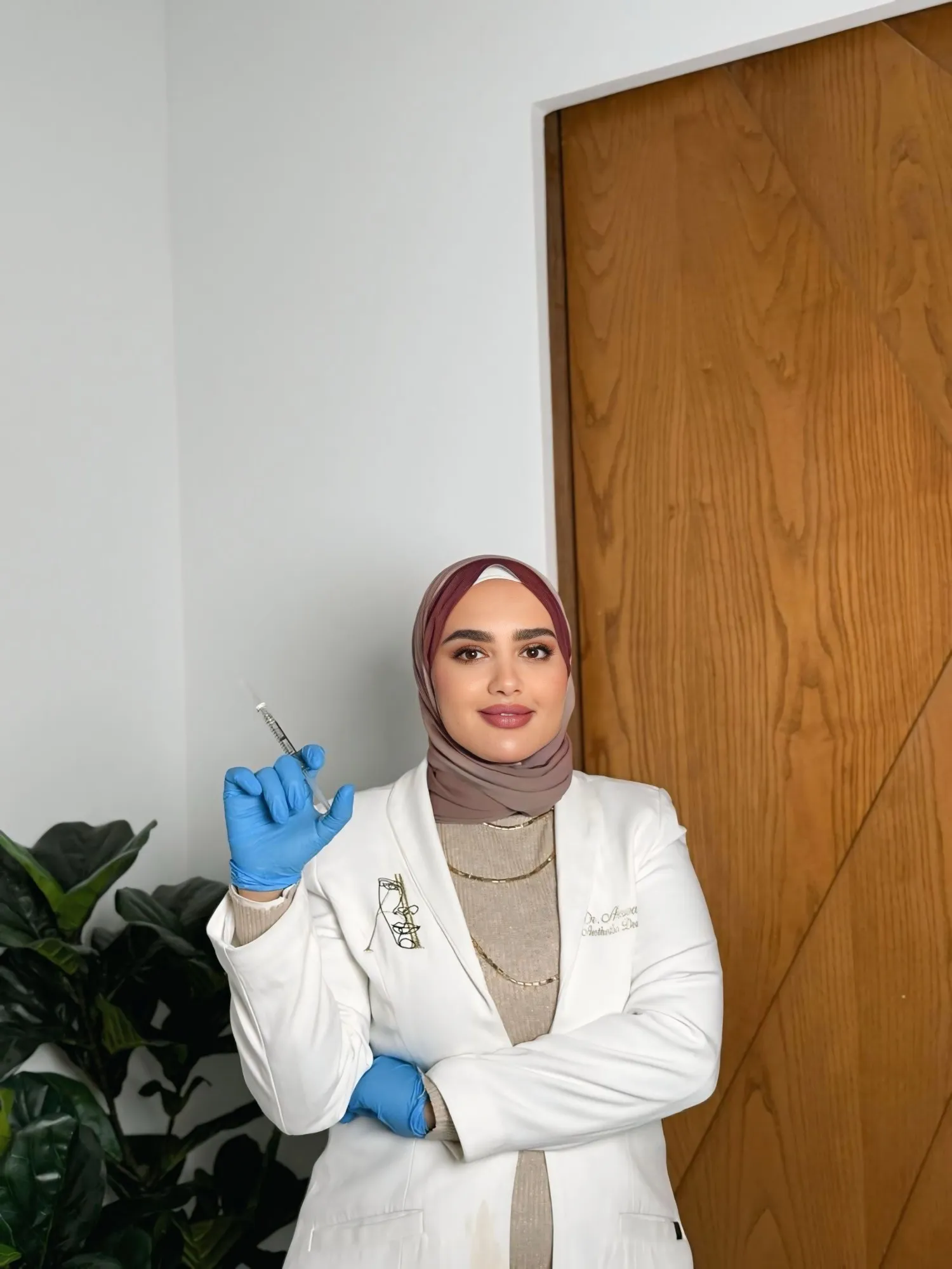 Dr. Arwa Diab in a white coat and blue gloves at the clinic