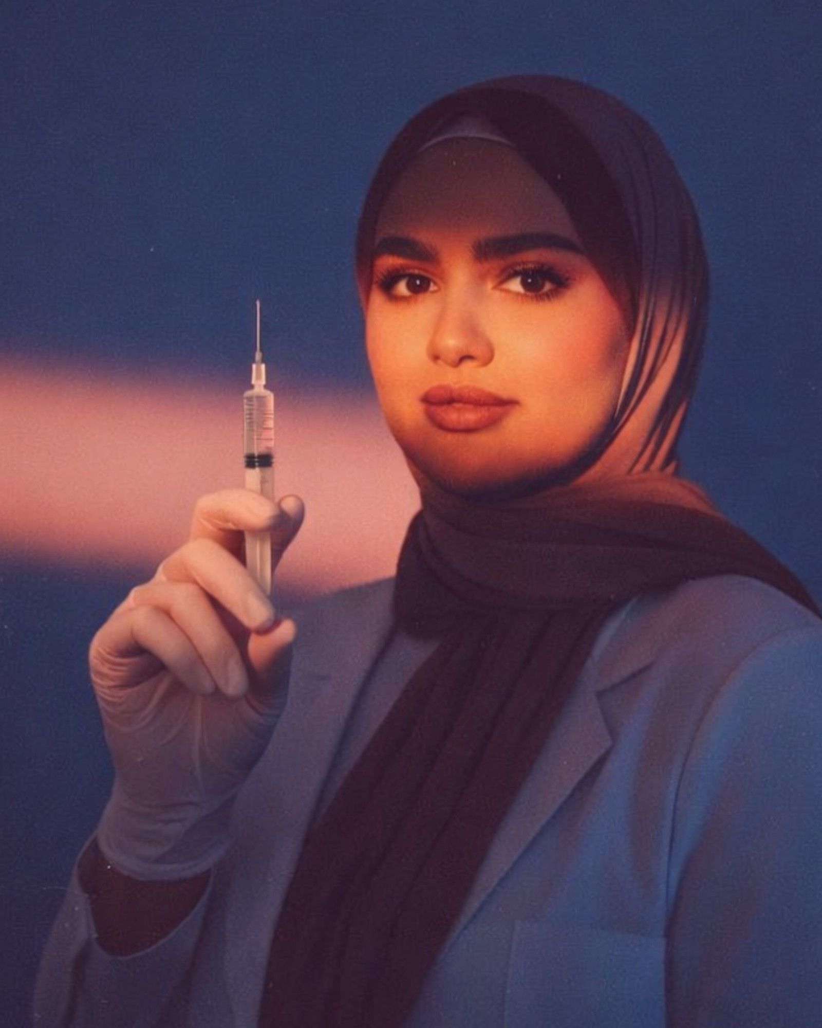 Dr. Arwa Diab in a blue blazer and hijab, holding a syringe, lit by a soft peach light