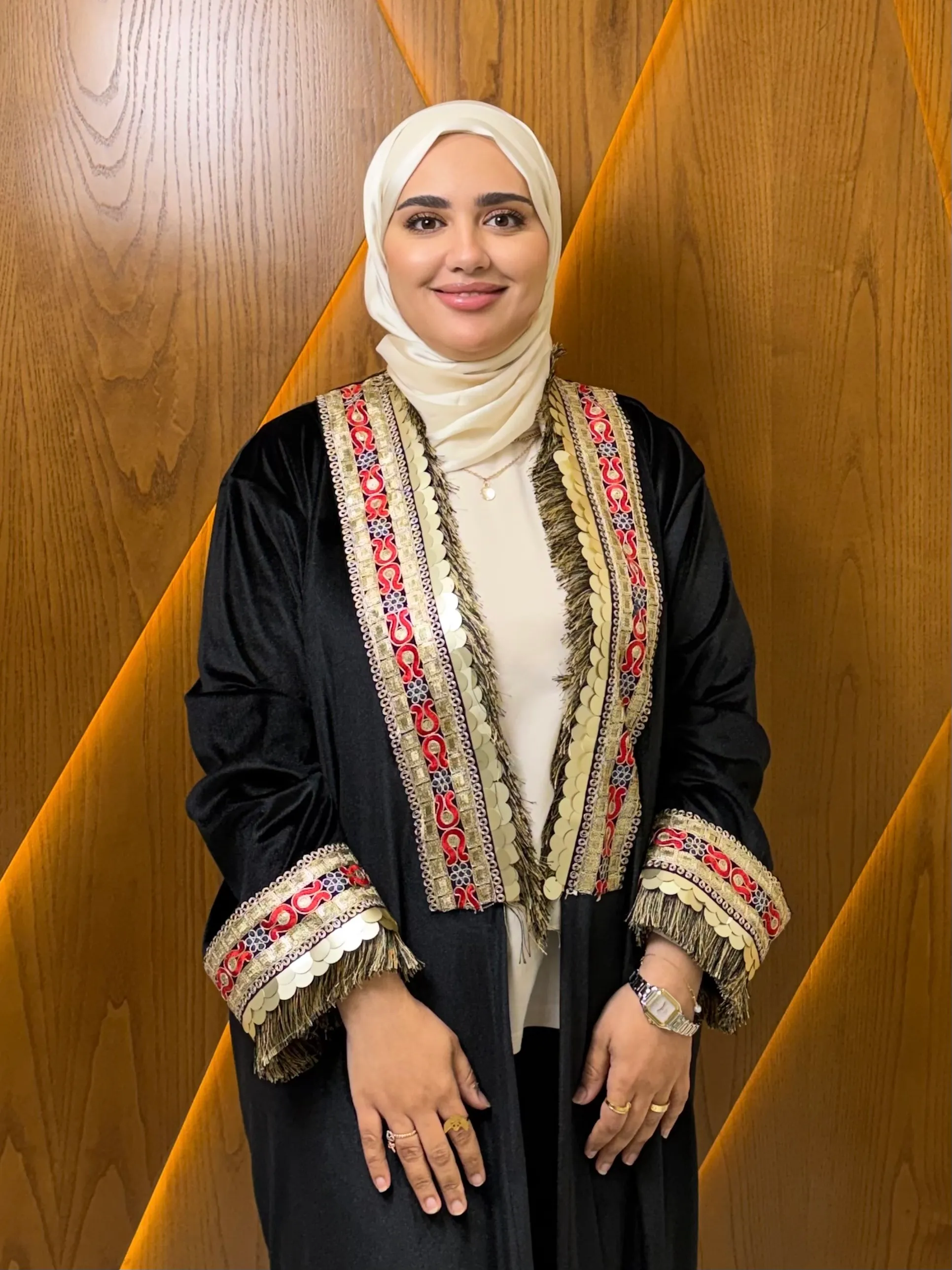 Dr. Arwa Diab smiling in a black abaya with traditional gold and red embroidery